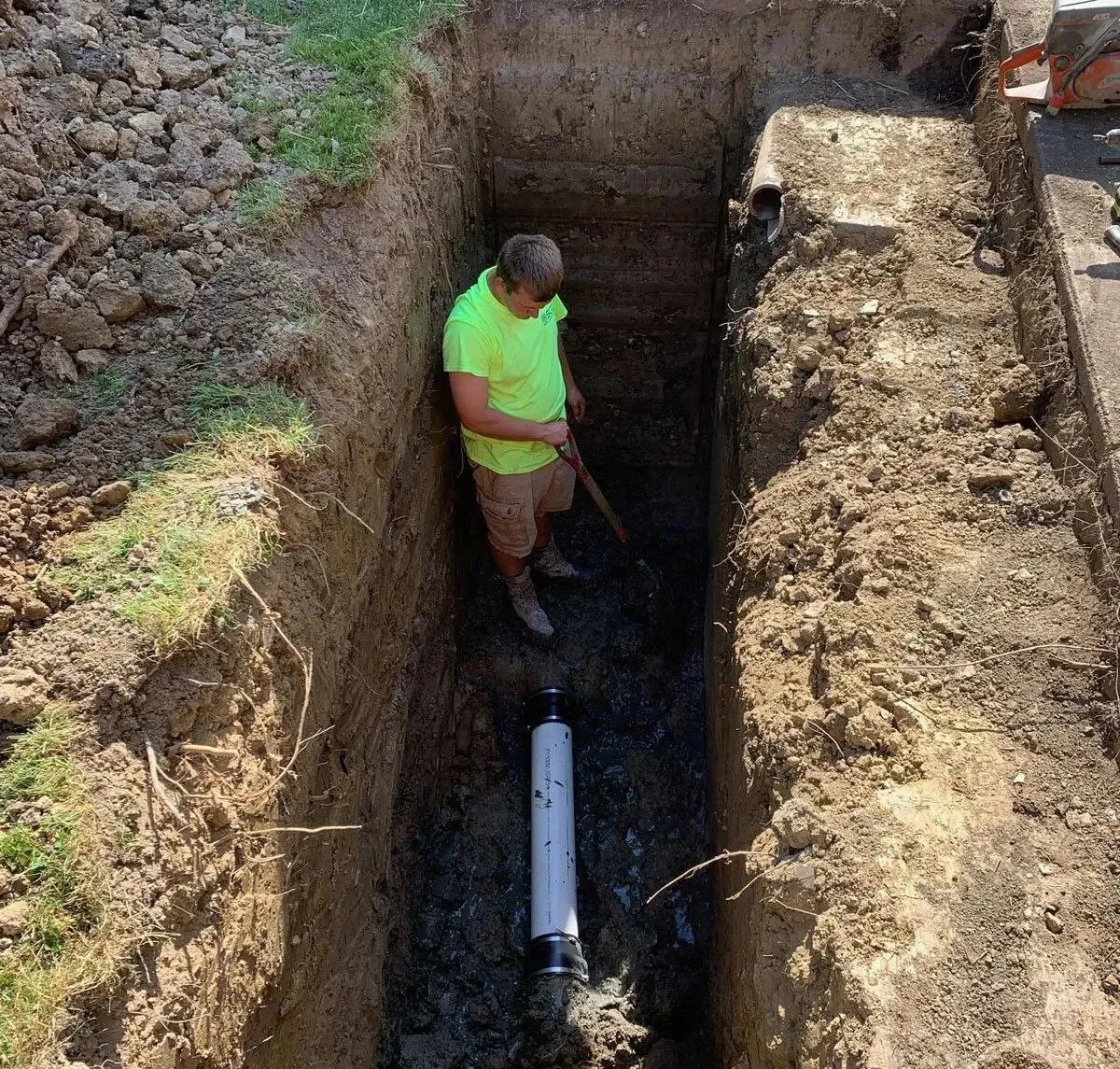 Professional plumbing technician standing in a deep trench during a full residential sewer line repair and replacement